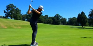 Golfer swinging driver on a sunny golf course.