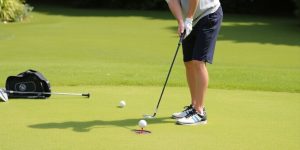 Golfer chipping in backyard with clubs and target nearby.